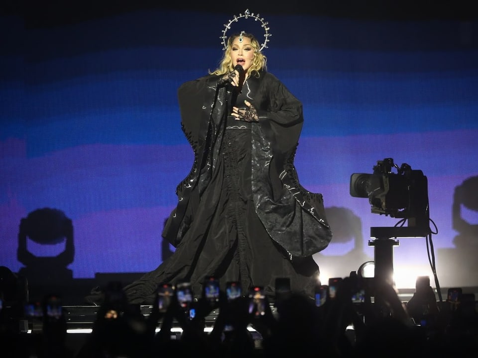 Sängerin in schwarzem Outfit und Kopfschmuck singt auf Konzertbühne vor Publikum.