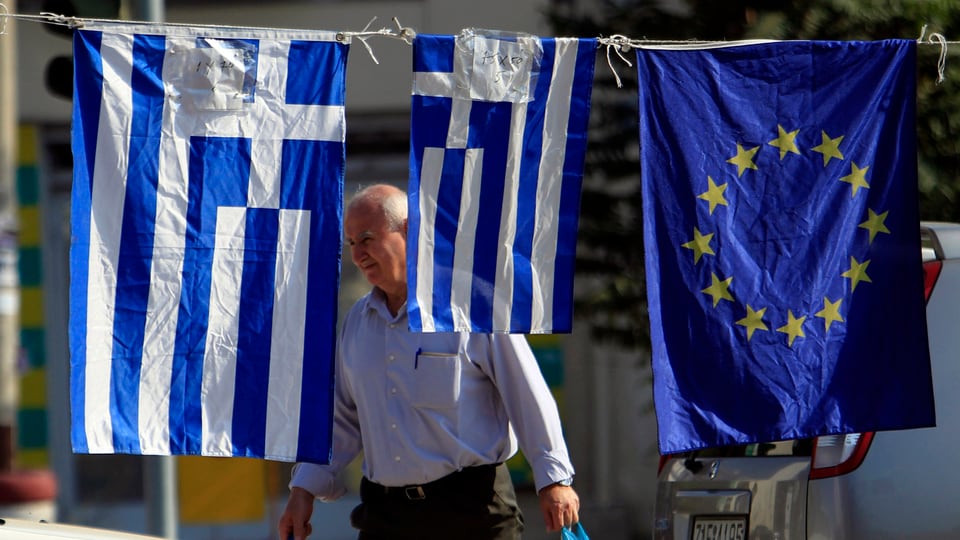 Die griechische Fahne hängt neben der EU-Fahne, dahinter geht ein Mann.