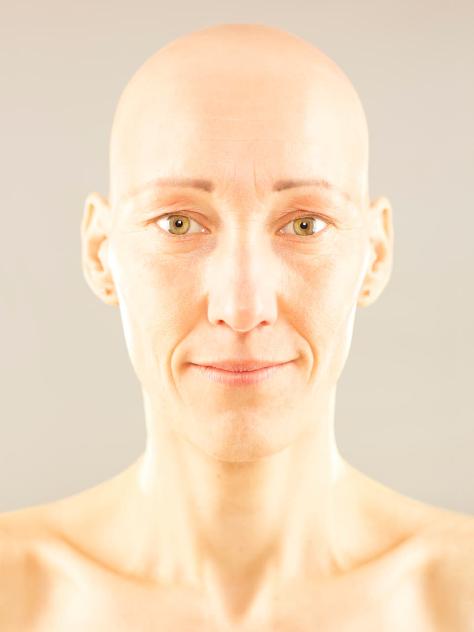 Porträt: Nahaufnahme einer Frau mit Glatze vor grauem Hintergrund.