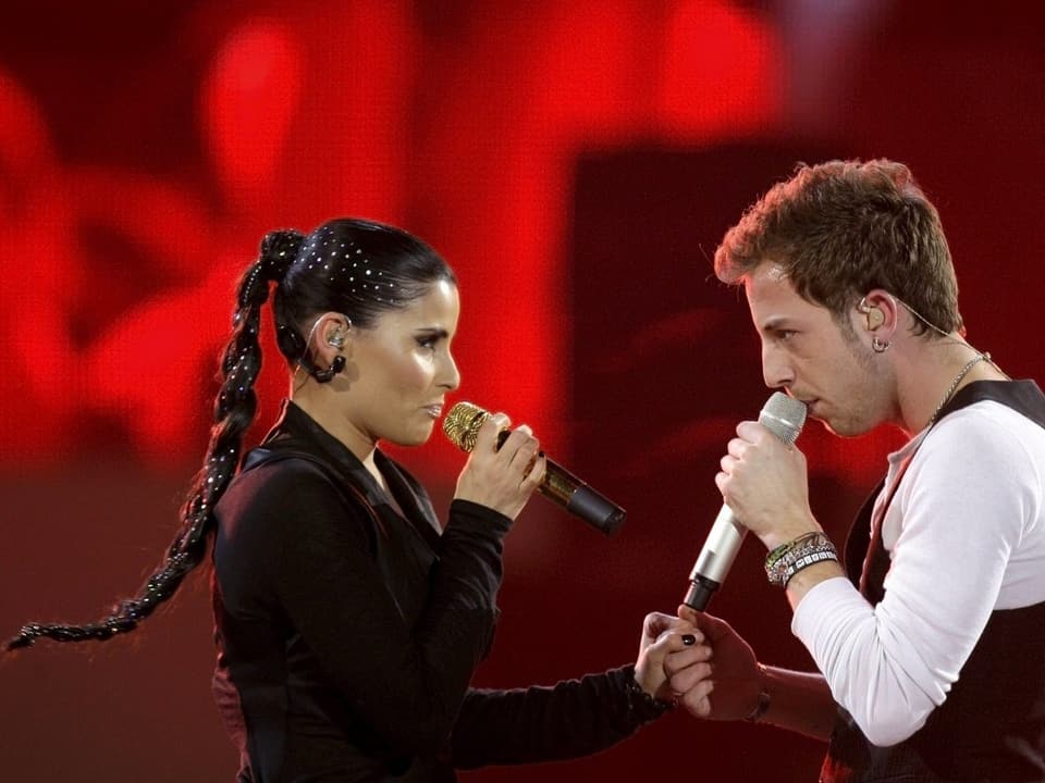 Nelly Furtado in schwarzem Dress hält die Hand von James Morrison, während beide singen.