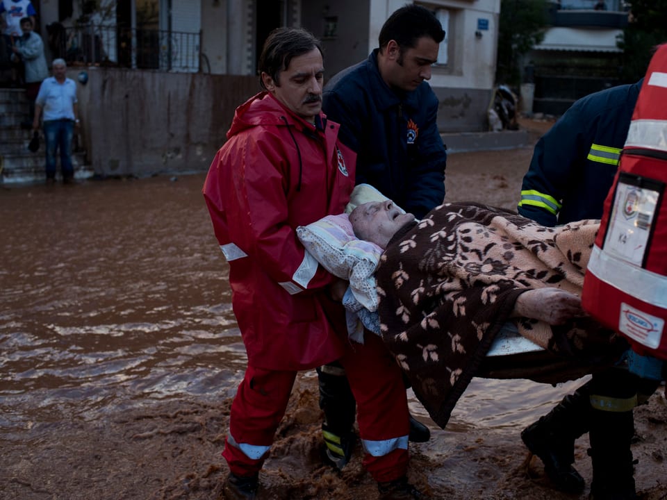 Rotkreuz-Helfer und Feuerwehrleute bergen einen alten Mann in der Stadt Mandra westlich von Athen.