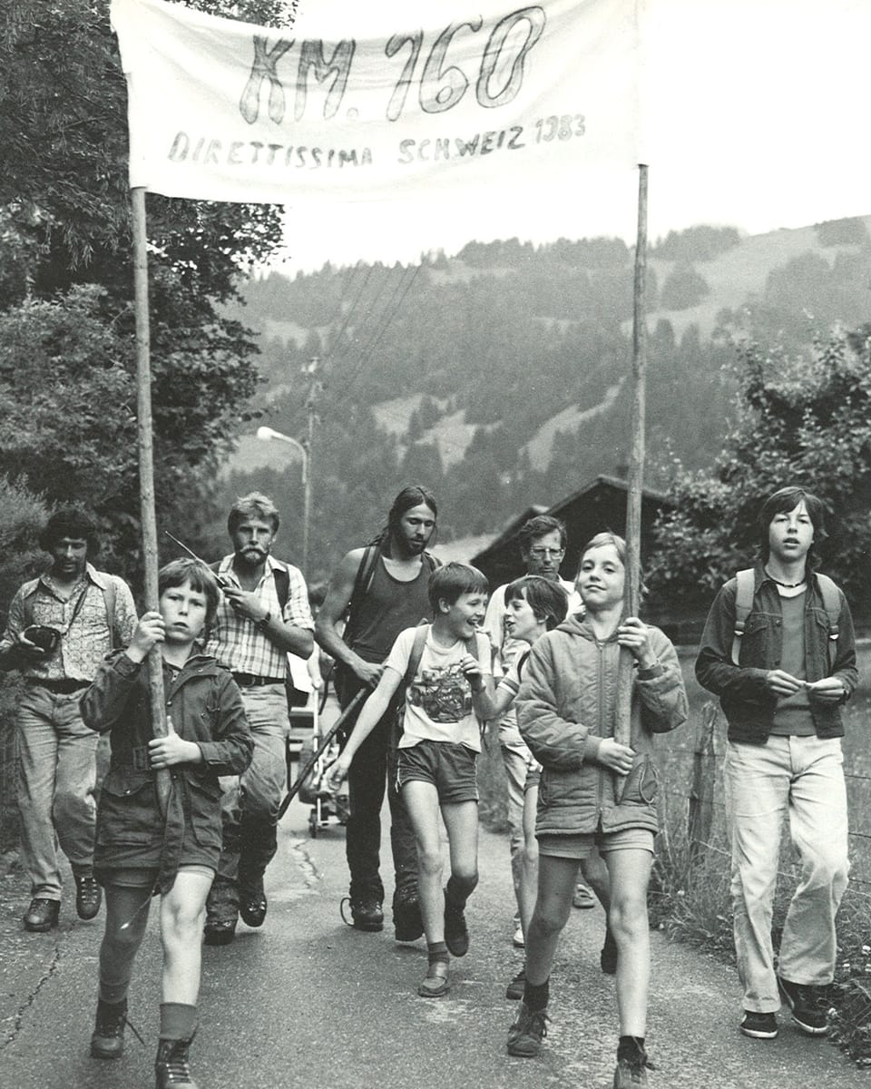 Ein paar Schüler halten ein Transparent mit der Aufschrift «KM 160» und begleiten Markus Liechti und Kurt Saurer Richtung Dorf.