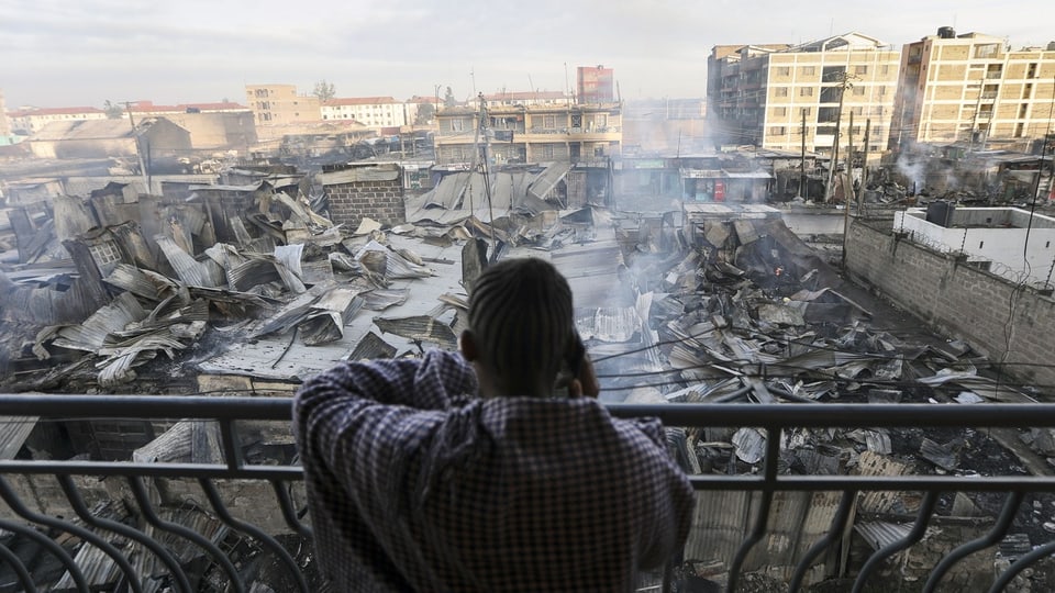 Person auf Terrasse blickt auf Trümmer von Gebäuden