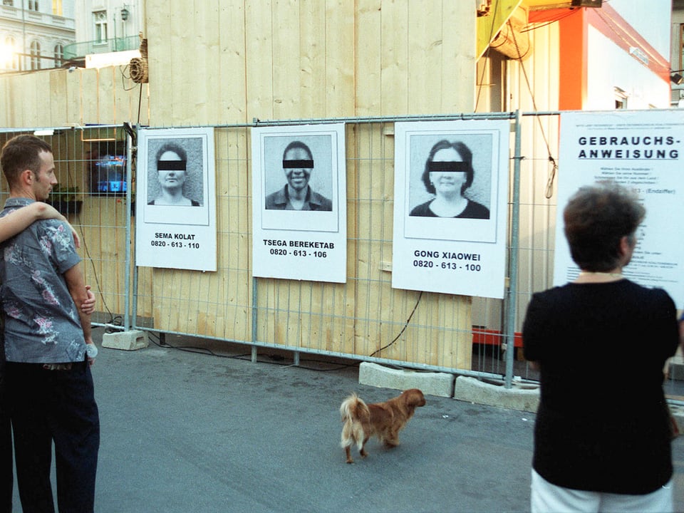 Plakate von «Asylbewerbern», die einen schwarzen Balken über den Augen haben, hängen an einem Container.
