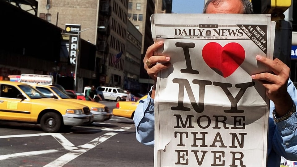 Ein Mann liest Zeitung. Sein Gesicht ist verdeckt von der Schlagzeile «I Love New York more than ever».