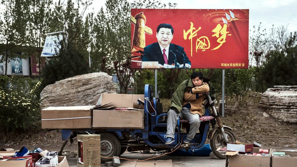 Ein Händler präsentiert seine Waren, im Hintergrund ein Plakat, auf dem Ministerpräsident Xi Jinping zu sehen ist.