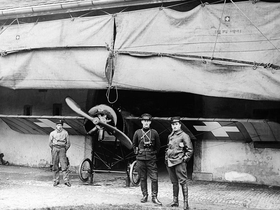 1914 Schwarz-Weiss-Aufnahme: Zwei Piloten und ein Unbekannter vor einem Flugzeug.