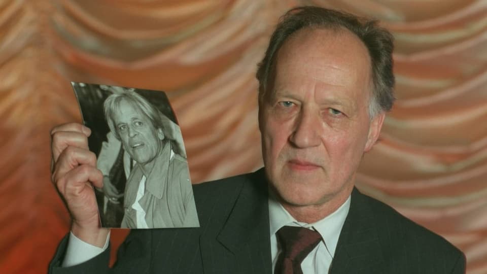 Herzog holding a portrait of Klaus Kinsky with a serious expression.