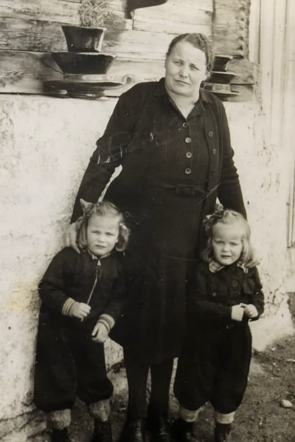 Stattliche, schwarz gekleidete Frau mit Zwillingen an ihrer Seite.