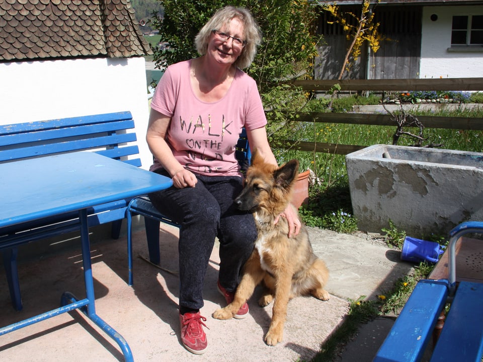 Die Autorin sitzt mit ihrem Hund auf einem Gartensitzplatz an einem blauen Tisch.