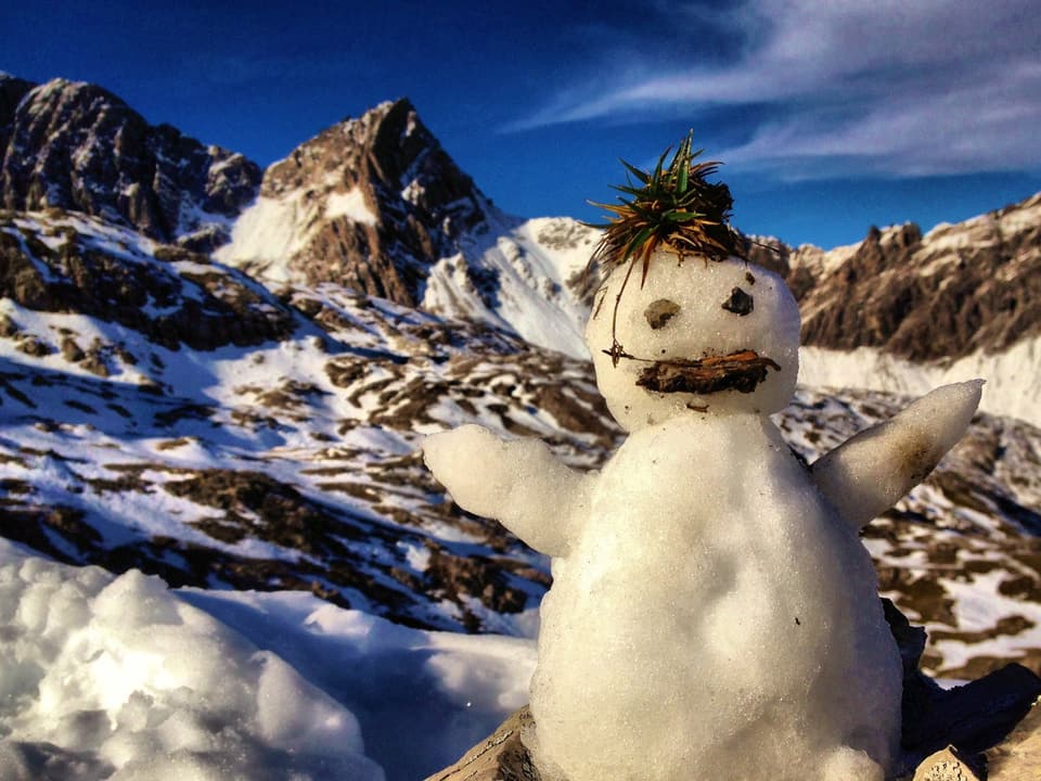 Ein Schneemann vor einem Bergpanorama.