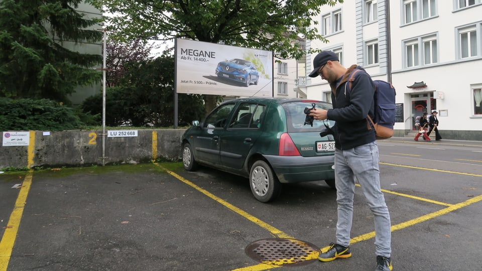 Ein Mann mit Kappe fotografiert einen Guilldeckel auf einem Parkplatz.