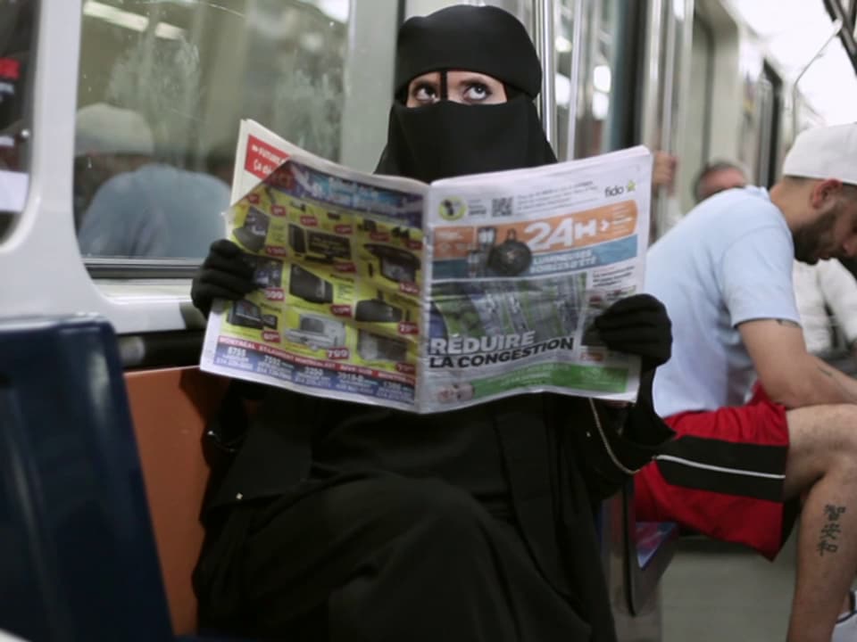 Ein Frau in Burka sitzt in einer U-Bahn und liest Zeitung