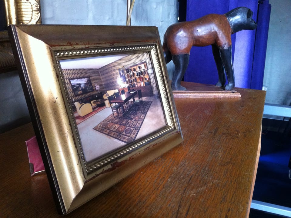 Ein Foto eines Bestattungsinstitutes steht, golden gerahmt, auf einem Schreibtisch.