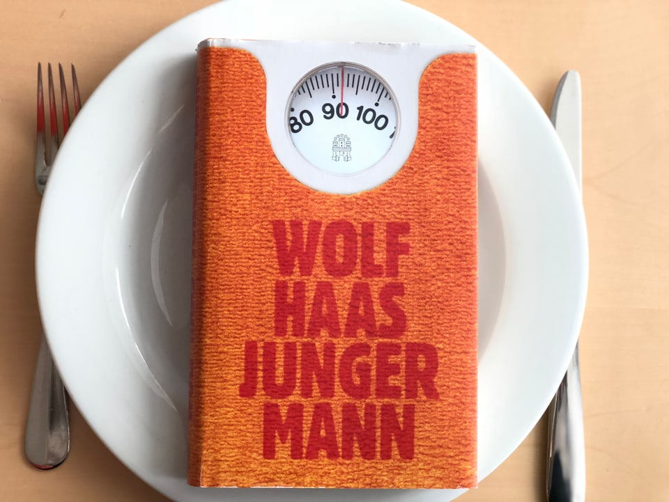 Der Roman «Junger Mann» von Wolf Haas liegt auf einem weissen Teller. Messer und Gabel daneben. 