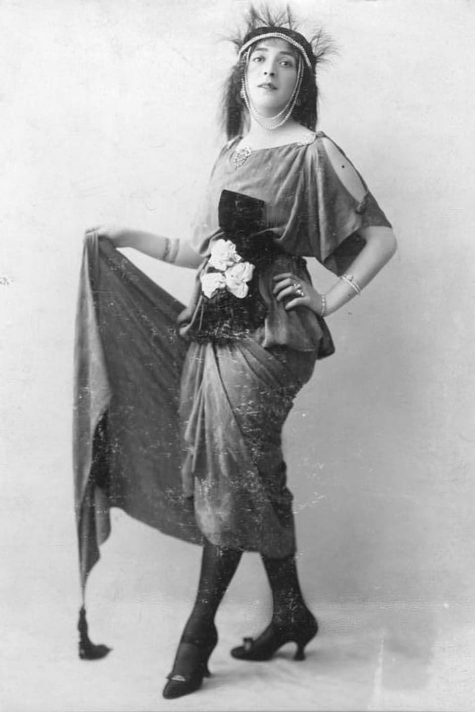 Frau in Kostüm mit wallendem Rock, Stiefeletten und Blumenbouquet um den Bauch gebunden. 