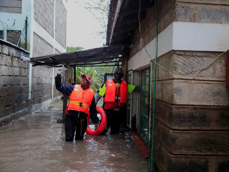 Rettungskräfte in Warnwesten stehen im überfluteten Strassenbereich neben einem Gebäude.
