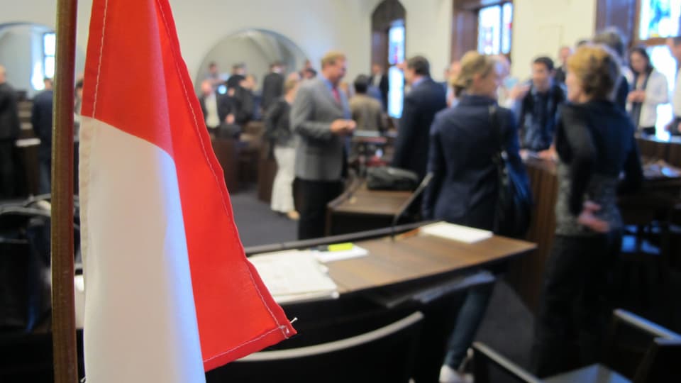 Blick in den Kantonsratssal Solothurn mit diskutierenden Personen unscharf im Hintergrund. Vorne eine Solothurn-Flagge.