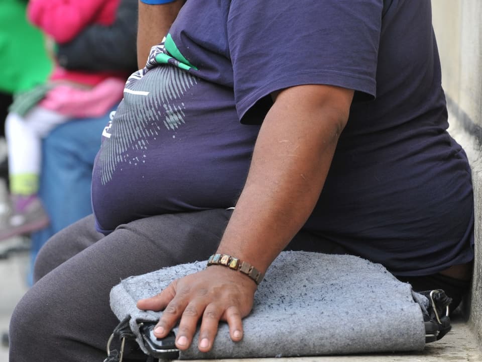 Ein stark übergewichtiger Mann sitzt auf einer Parkbank.