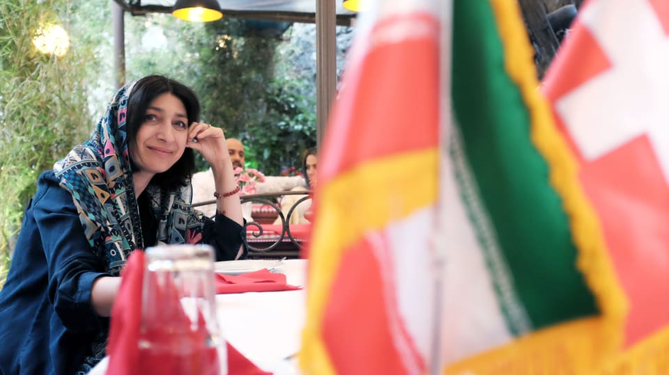 Eine Frau sitzt im Restaurant, im Vordergrund: die Iran und die Schweizer Flagge