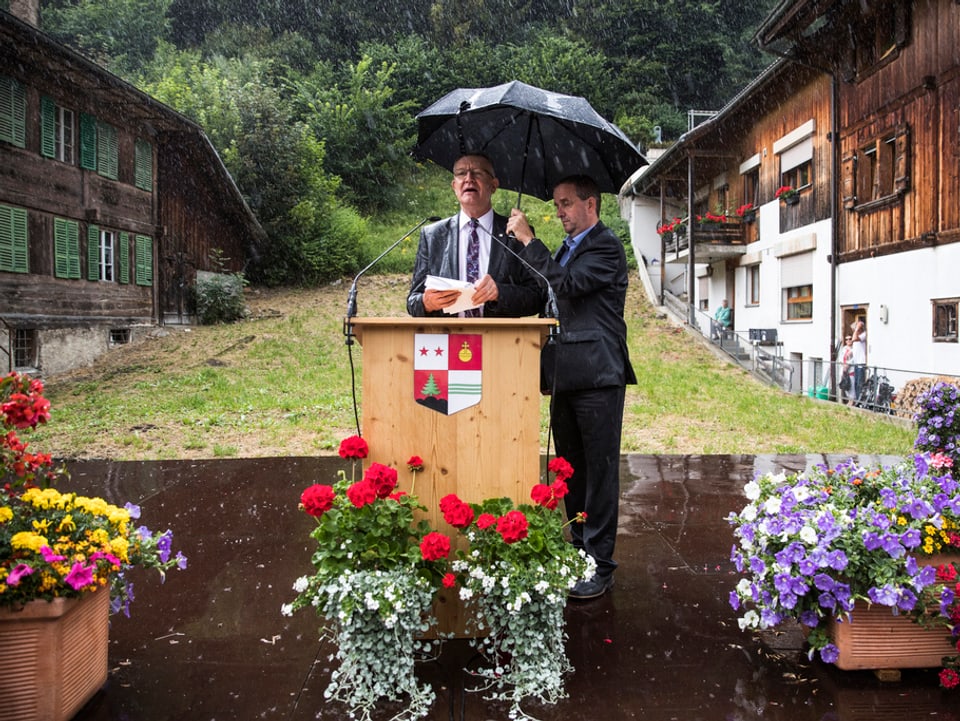 Bild vom Regierungspräsidenten, wie er mit einem Schirm vom Regen beschützt wird