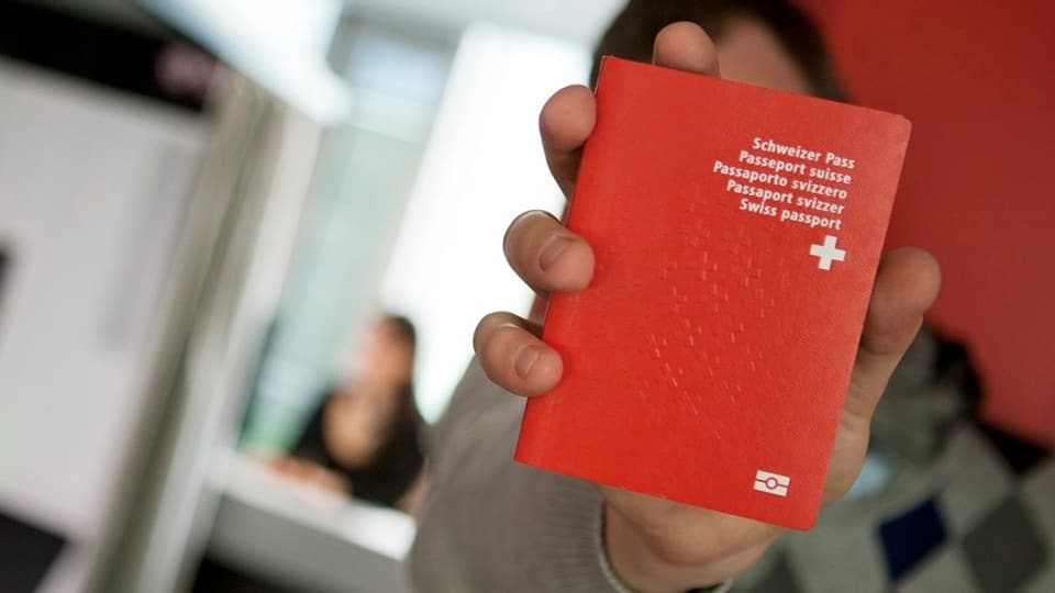 Ein Mann hält einen Schweizer Pass in die Kamera, sein Gesicht ist dahinter verborgen.