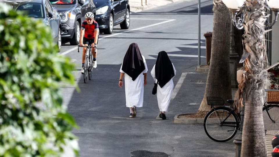 Zwei Nonnen laufen die Strasse entlang, ein Velofahrer kommt ihnen entgegen. 