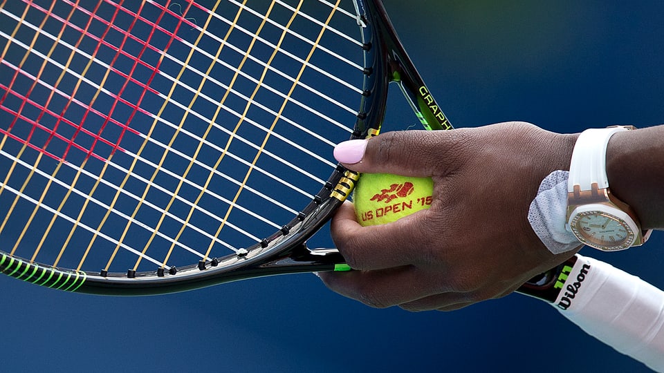 Tennisracket ist im Hintergrund.Im Vordergrund ist Serena WIlliams Hand mit Tennisball. Nägel sind rosa gefärbt.