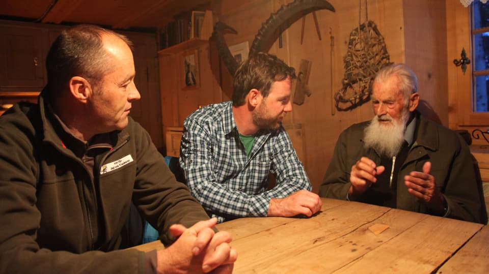 Nik Hartmann sitzt mit Wildhüter und altem. bärtigen Mann am Tisch. 