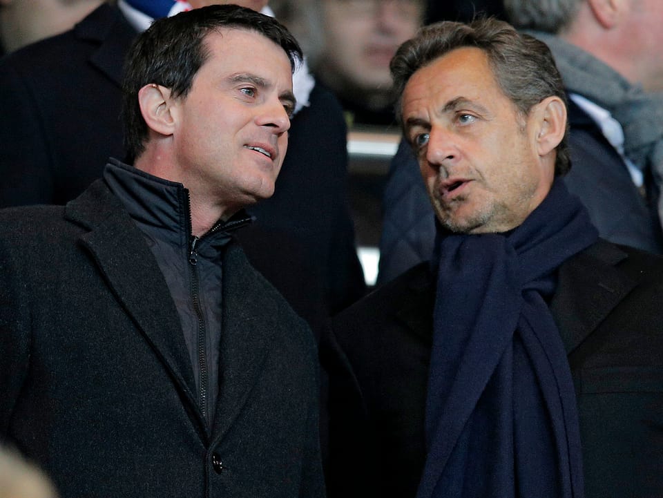 Manuel Valls (links) steht neben Nicolas Sarkozy (rechts) auf der Tribüne eines Fussballstadions und unterhalten sich.