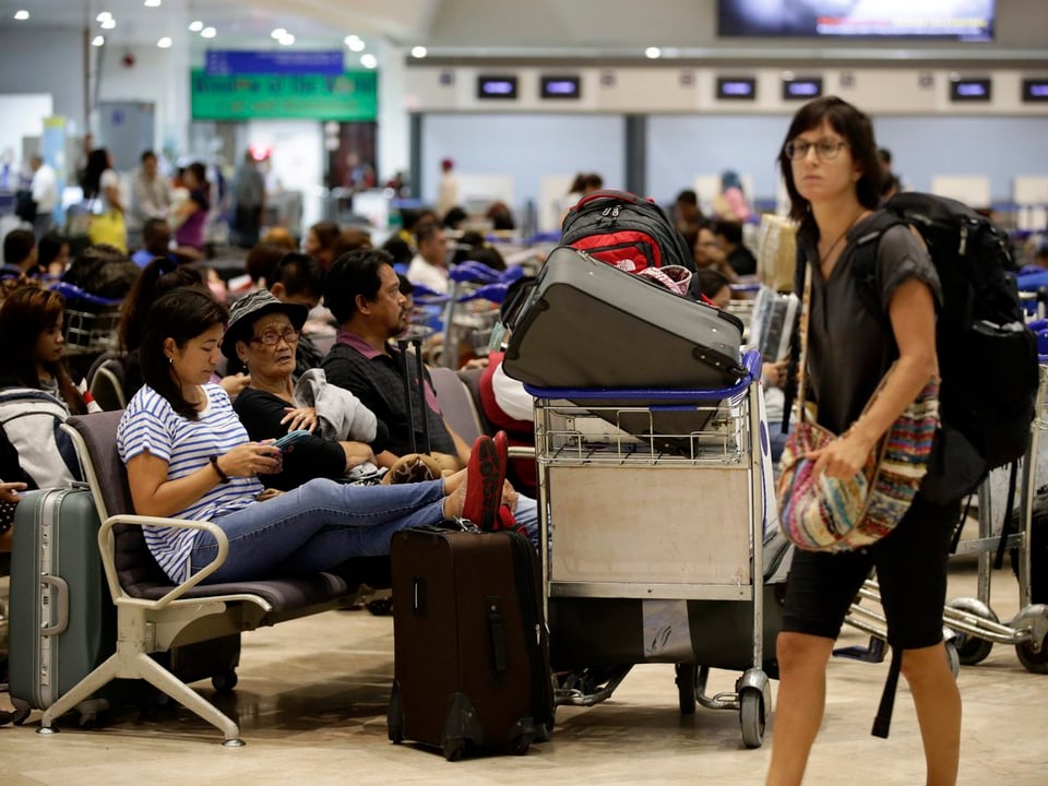 Gestandete Touristen sitzen in einer Wartehalle am Flughafen von Pasay City, rechts eine stehende Frau mit Rucksack