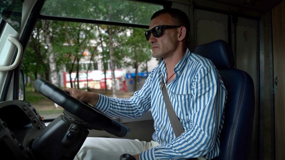 Mann in Streifenhemd am Steuer von Kleinbus.
