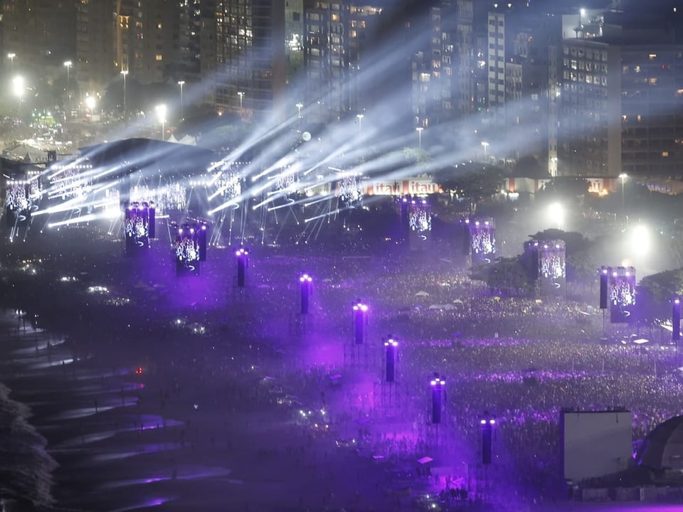 Nachtansicht eines belebten Musikfestivals mit Lichtshows und Menschenmenge in einer Stadt.