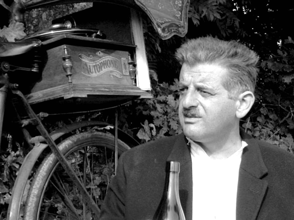 Ein Mann sitzt vor seiner Bierflasche, dahinter steht ein Fahrrad.