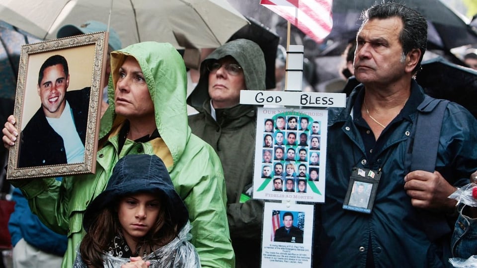 Eine Familie in Regenkleidung hält Bilder Verstorbener hoch