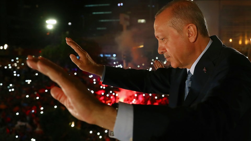 Erdogan mit erhobenen Händen in der Nacht, unten viele Lichter von Anhängern.
