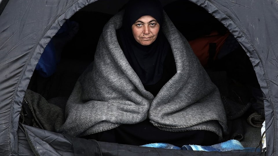 Frau sitzt mit Decke in einem Zelt.