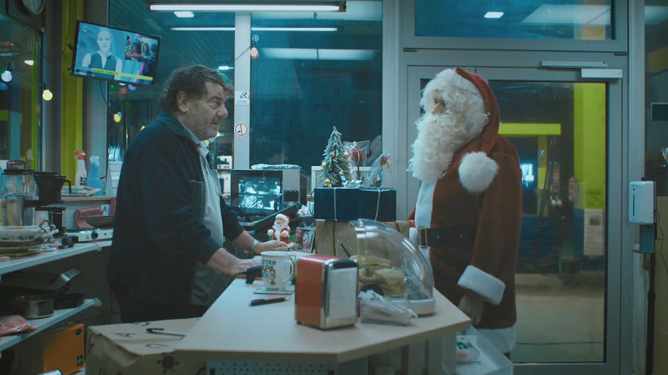 Ein Mann und Santa Clause stehen sich an einer Theke gegenüber. 