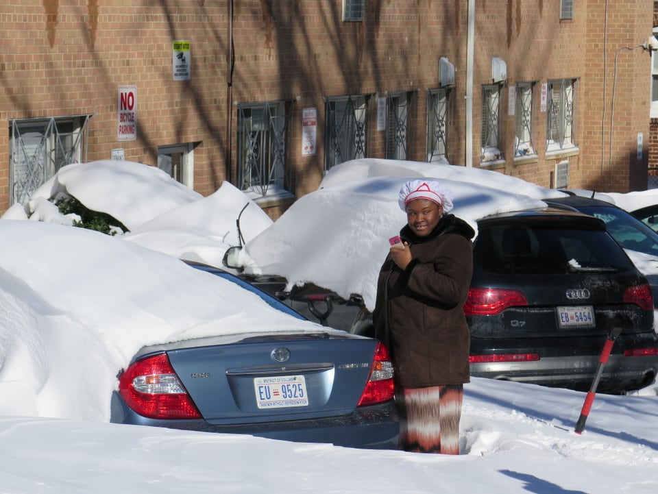Eine Frau steht vor einem eingeschneiten Auto 