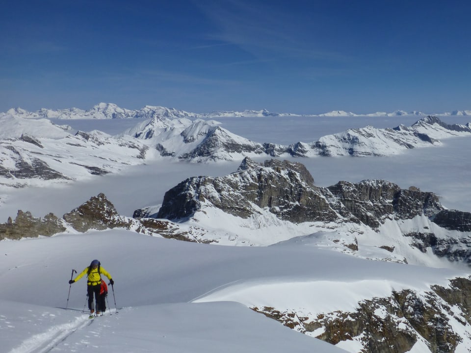 Skitüreler unterwegs vor vielen Gipfeln, die aus dem Nebelmeer ragen. 