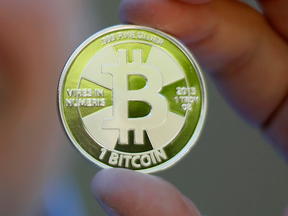 Ein zur Münze gemachter Bitcoin zwischen Daumen und Zeigefinger einer nicht zu sehenden Person.