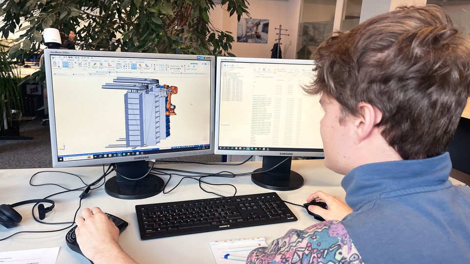 Ein junger Mann mit braunen Haaren sitzt an einem Arbeitsplatz mit zwei Bildschirmen, ein CAD-Programm ist geöffnet
