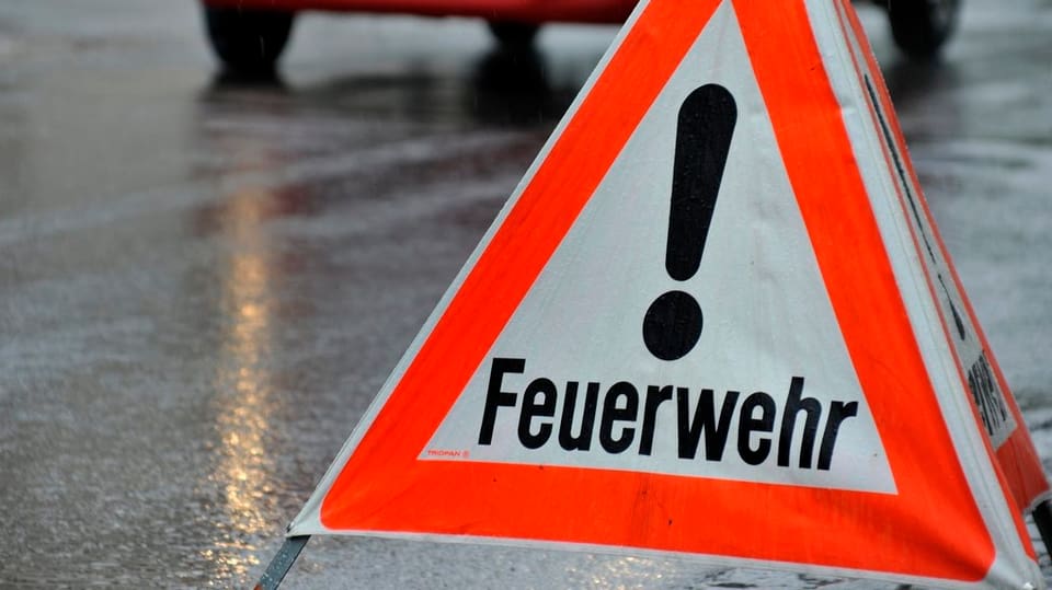 Dreibeiniges, dreieckiges "Achtung Feuerwehr"-Signal steht auf nasser Strasse.