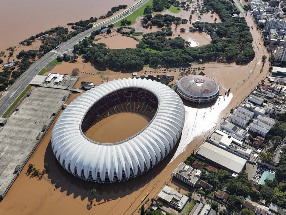 Luftbild eines ovalförmigen Stadions und dessen Umgebung. Hochwasser hat die Strassen und den Innenbereich überflutet.