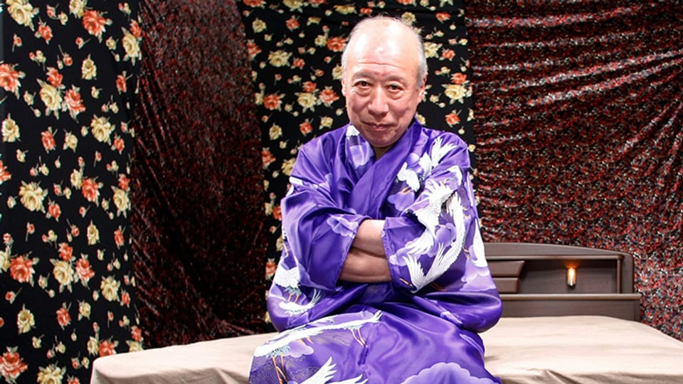Ein Mann sitzt in einem Kimono auf einem Bett.