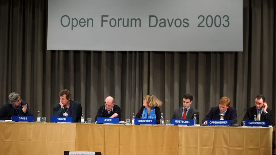 Sieben Personen sitzen hinter ihrem Mikrofon. Oberhalb ist ein Schriftzug mit «Open Forum WEF» zu sehen.