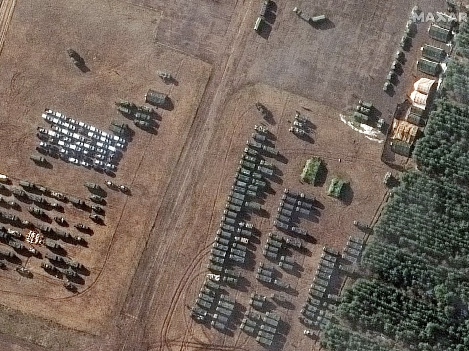 Vogelperspektive: Militärfahrzeuge stehen auf einem Feld neben einem Wald.