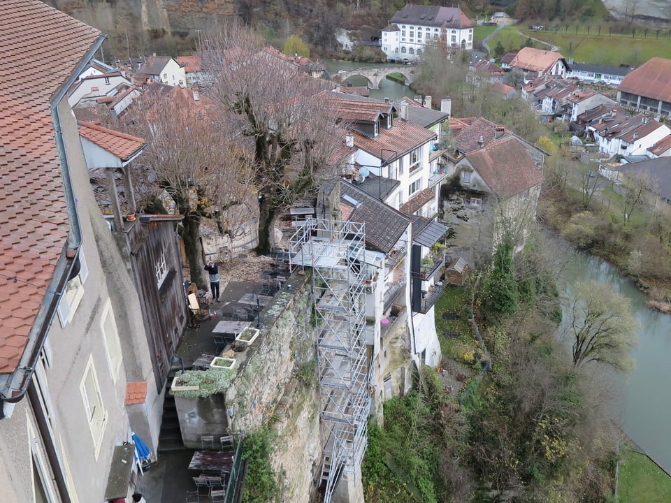 Blick von oben auf Häuser, die am Rand der steilen Felswand stehen. Unten die Saane.