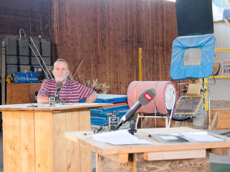 Daniel Haussener steht an einem Stehpult. Im Vordergrund ein zweites Stehpult, ebenfalls mit einem Mikrofon.