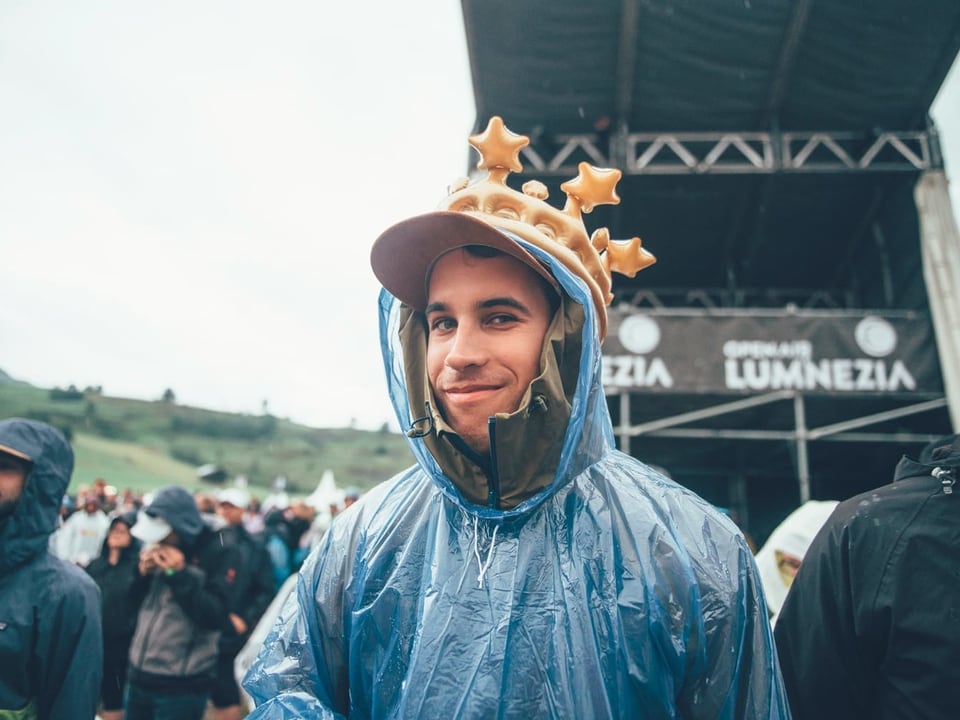 Mann mit aufblasbaren Krone und blauen Regenpellerine lächelt in die Kamera